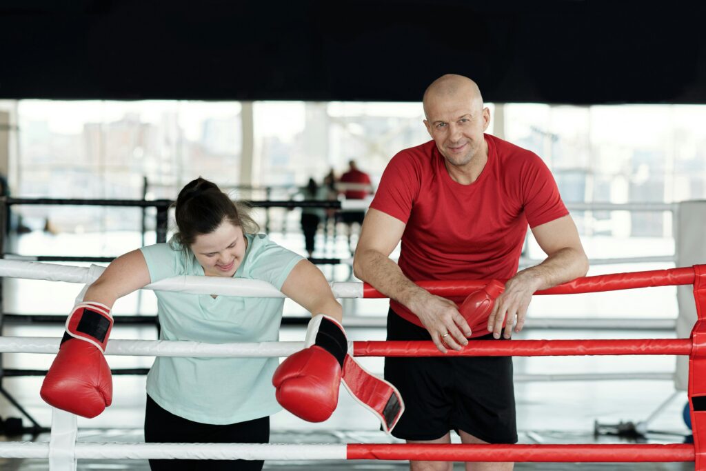 Man and woman enjoy a friendly boxing session in a gym, emphasizing inclusivity and fitness.