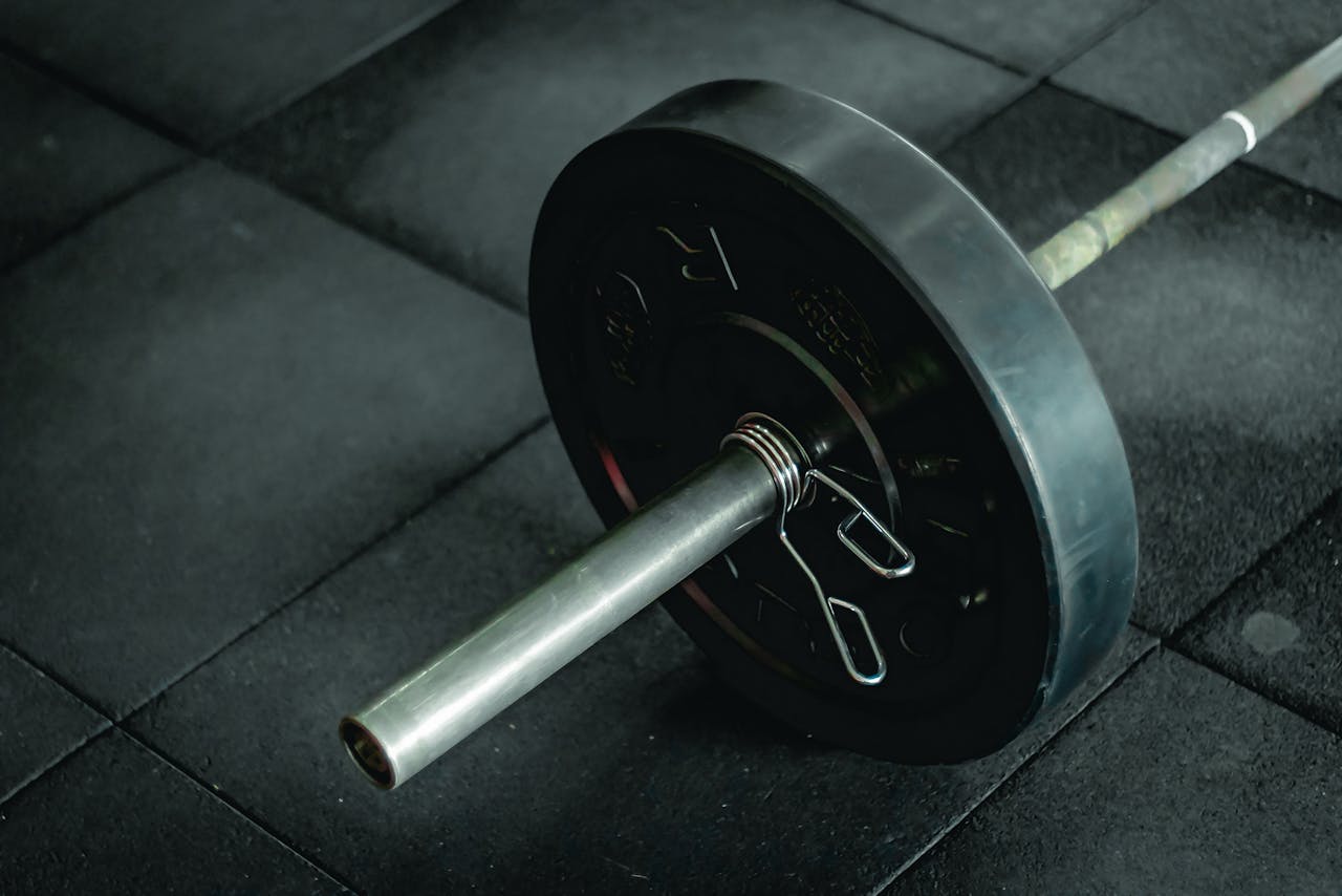 Detailed view of a barbell with heavy weights resting on a dark gym floor mat.
