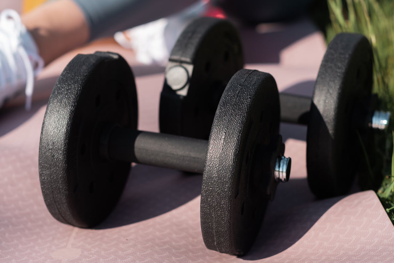 Black dumbbells on a pink exercise mat outdoors, ideal for fitness content.
